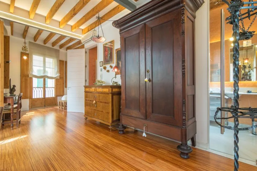 A warmly lit room with polished wood floors, exposed ceiling beams, and dark wood furnishings.