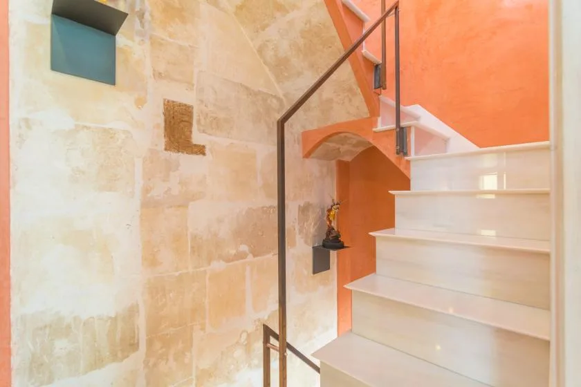 A staircase with white steps rises beside warm orange walls and pale stone.