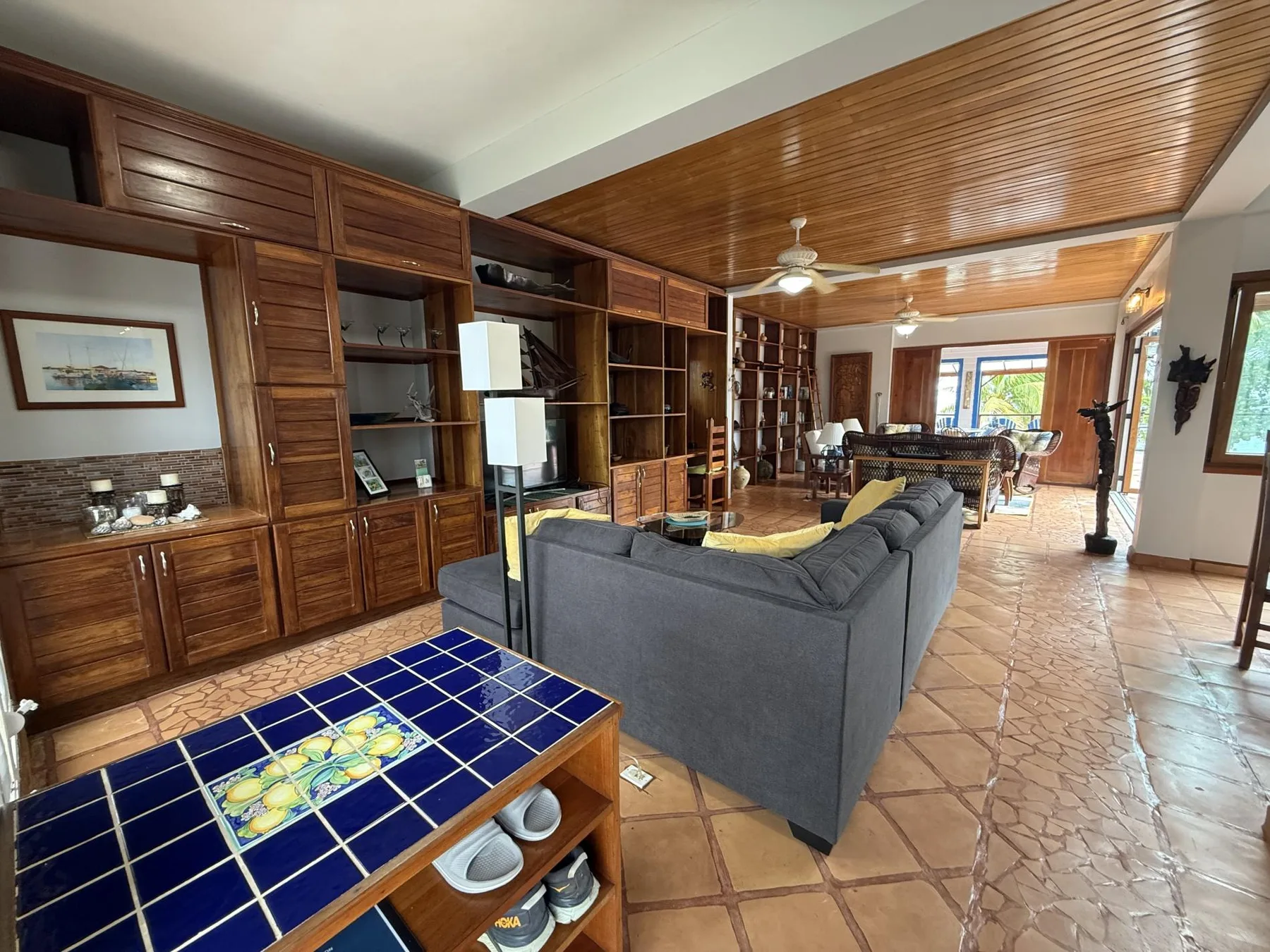 Una sala de estar con asientos grises, estanterías de madera y suelo de baldosas.