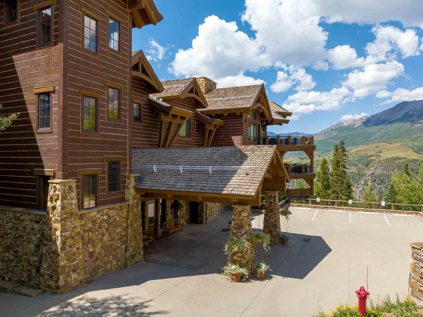 A lodge-style building with brown siding and stonework overlooks a mountain valley.