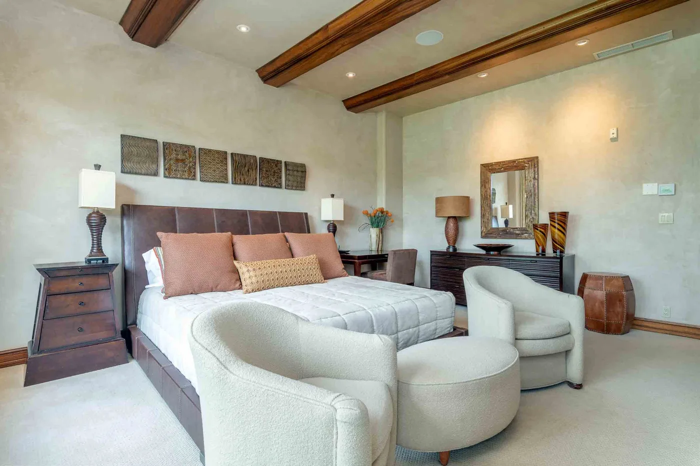 A bedroom with a bed, two upholstered chairs, and exposed wooden ceiling beams.