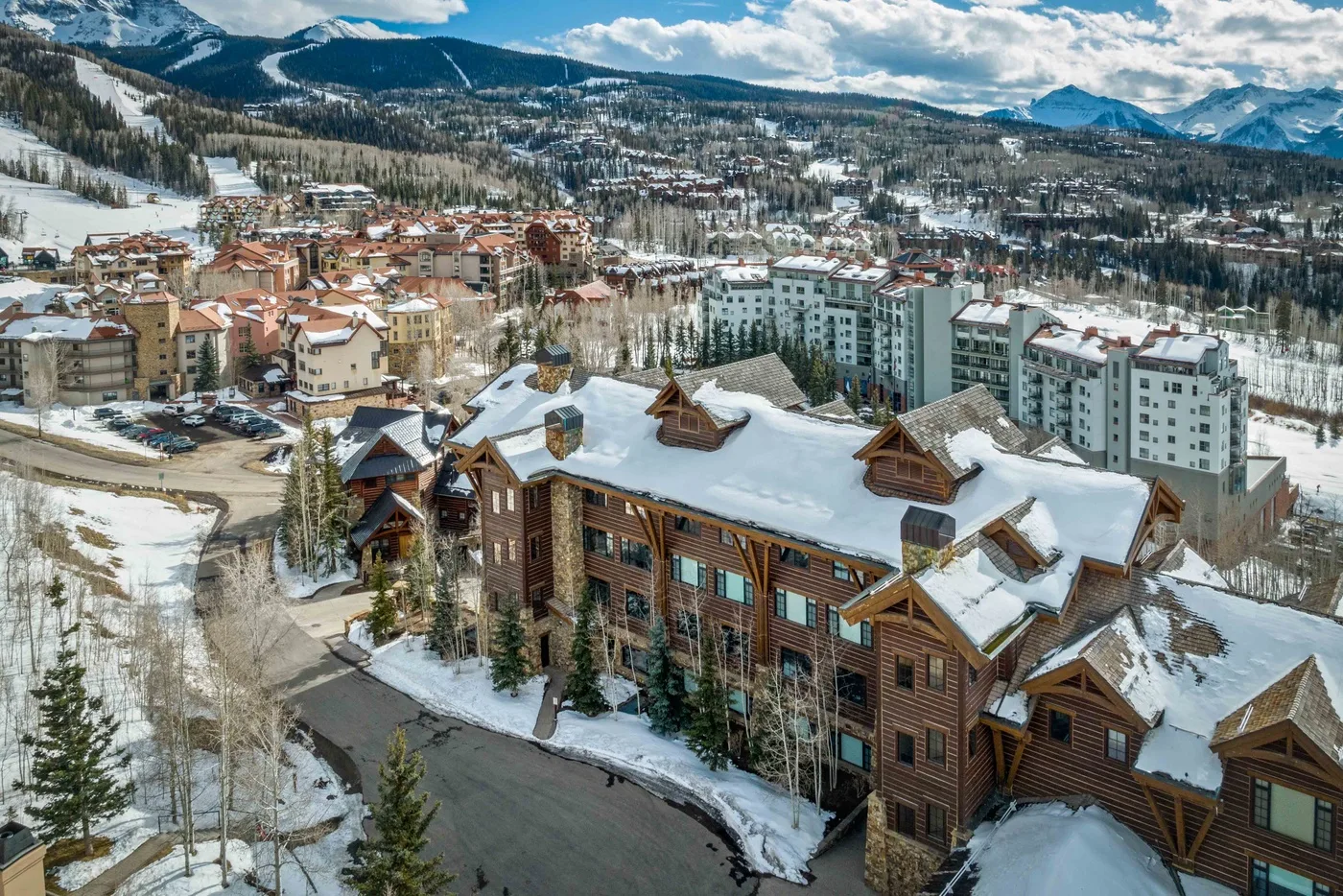 Snow-covered buildings sit among mountain slopes in a winter resort scene.