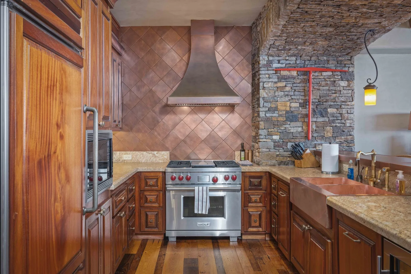 A rustic kitchen features wooden cabinets, a range, and a stone backsplash.