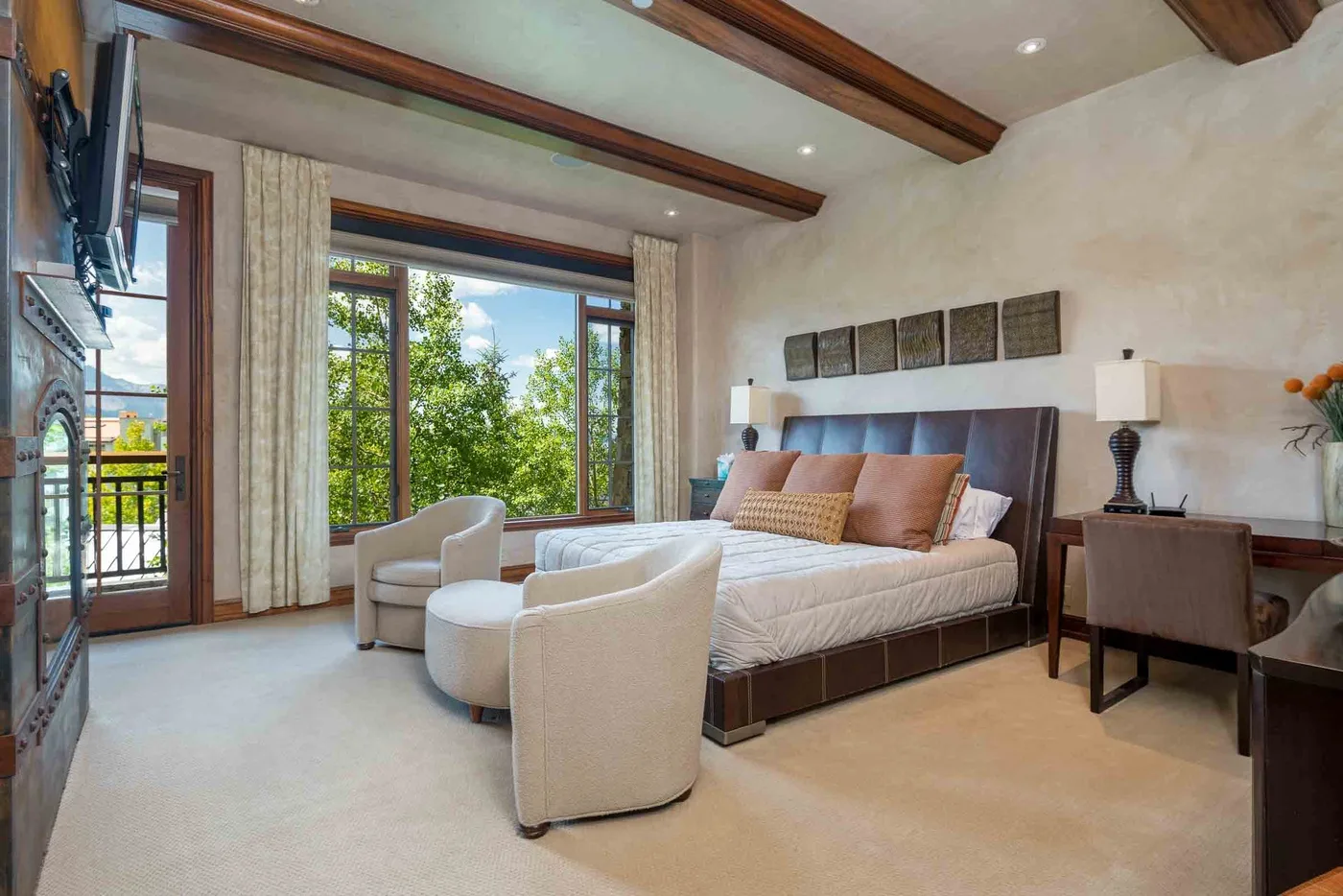 A bedroom with a bed, upholstered seating, and large windows overlooking greenery.