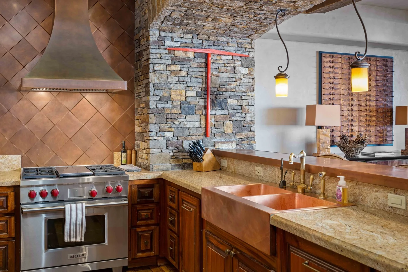 A rustic kitchen with a large stove, stone wall, and copper sink.