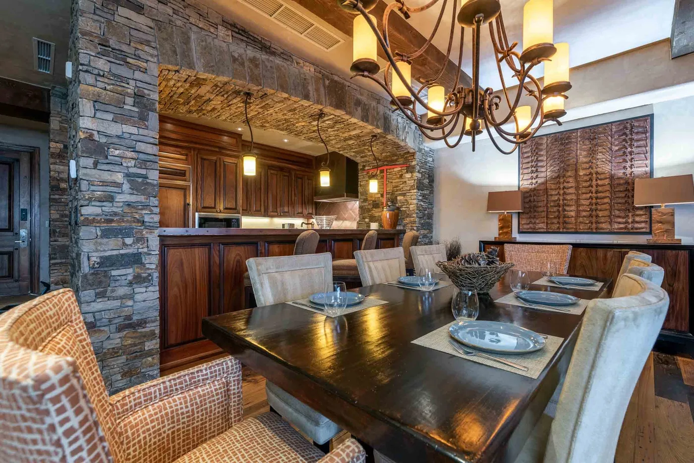 A dining area with a long table, upholstered seating, and a stone accent wall.