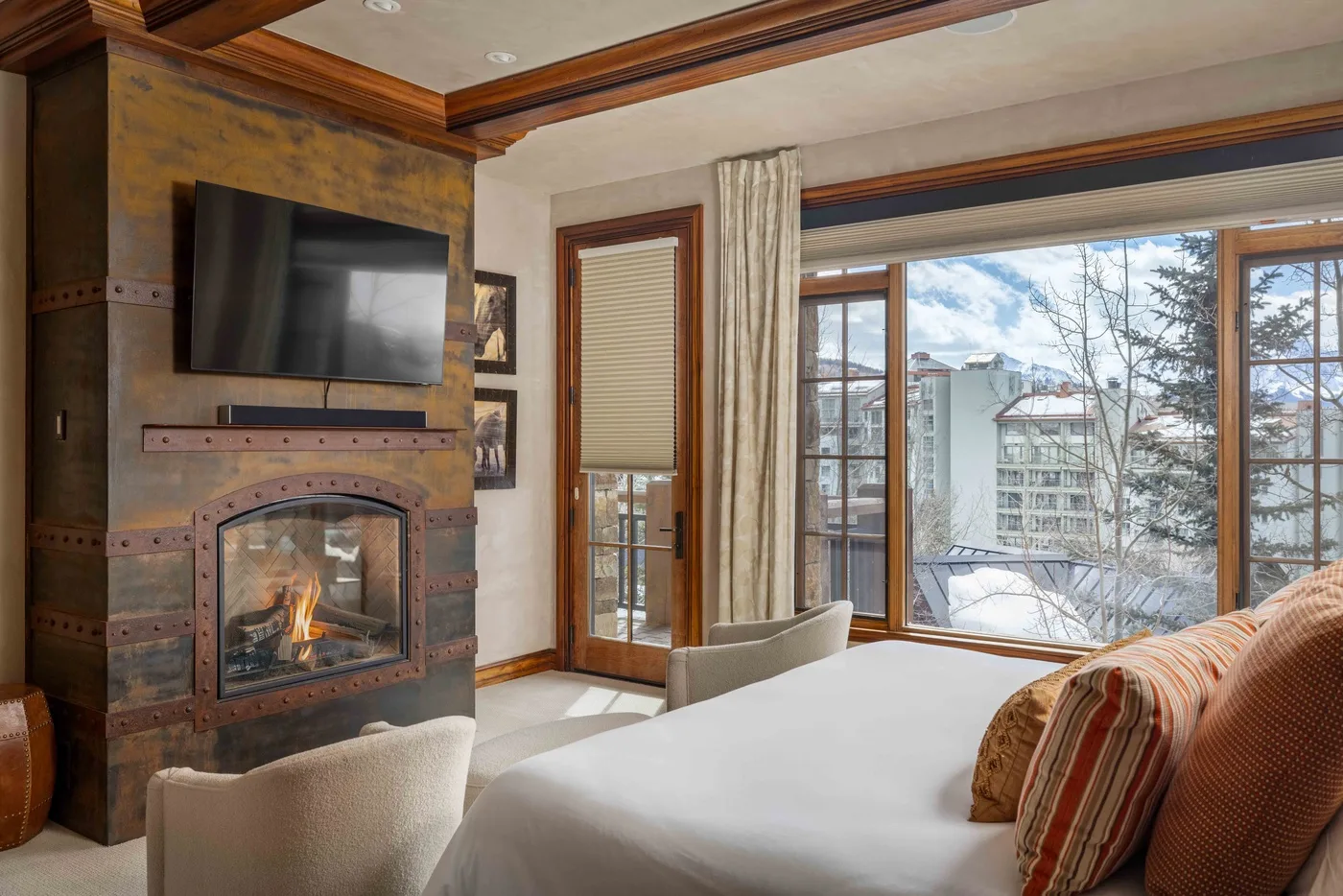 A bedroom with a bed, a fireplace, and large windows overlooking snowy trees.