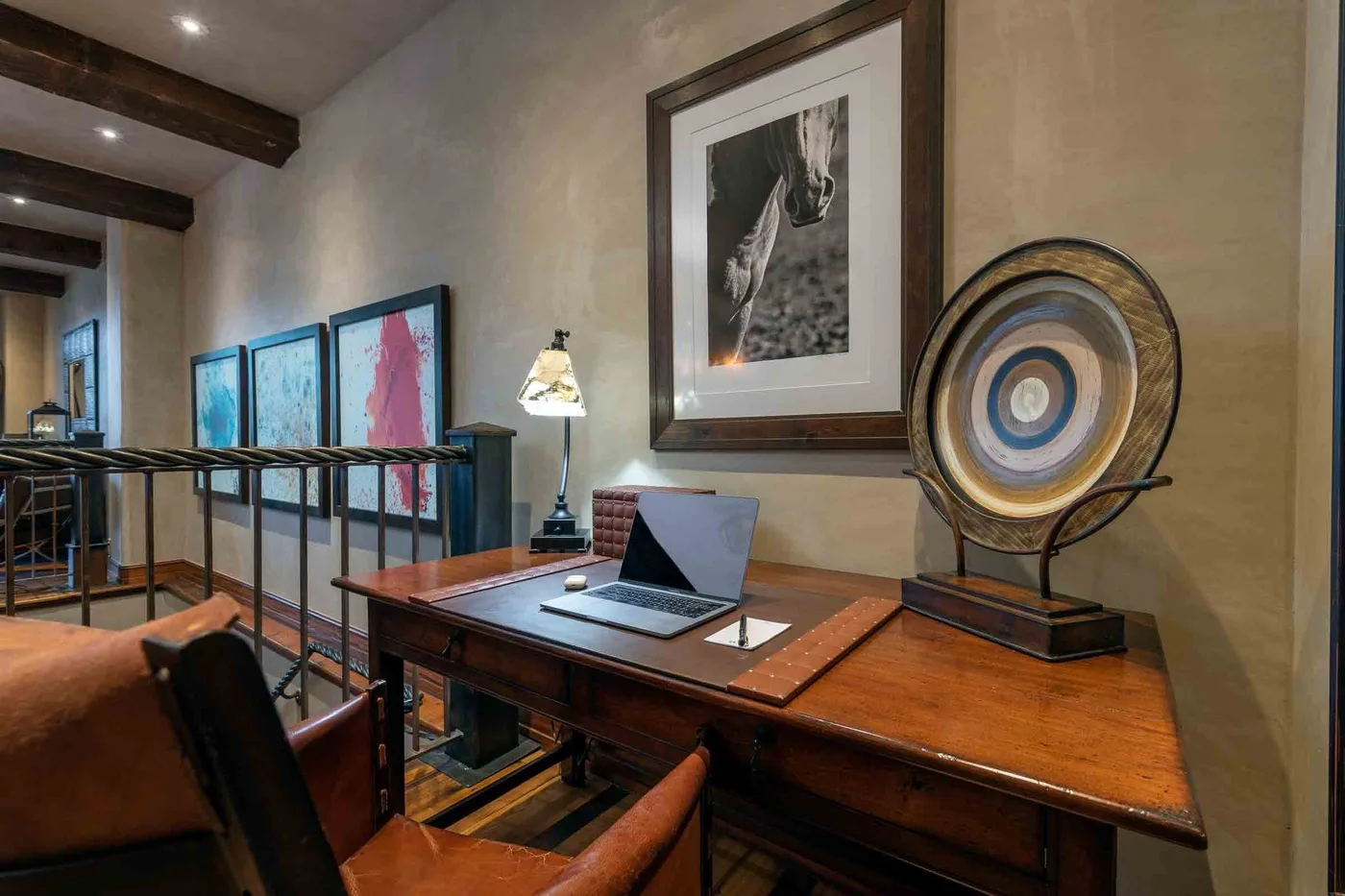 A study area with a wooden desk, laptop, and framed artwork.