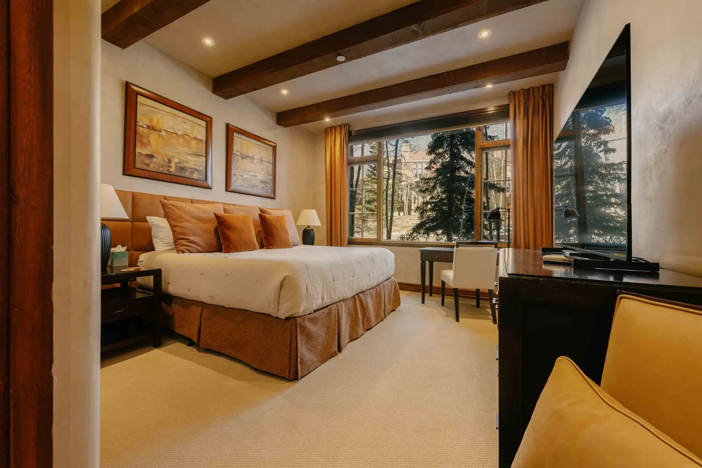 A bedroom with a large bed beside windows overlooking trees.