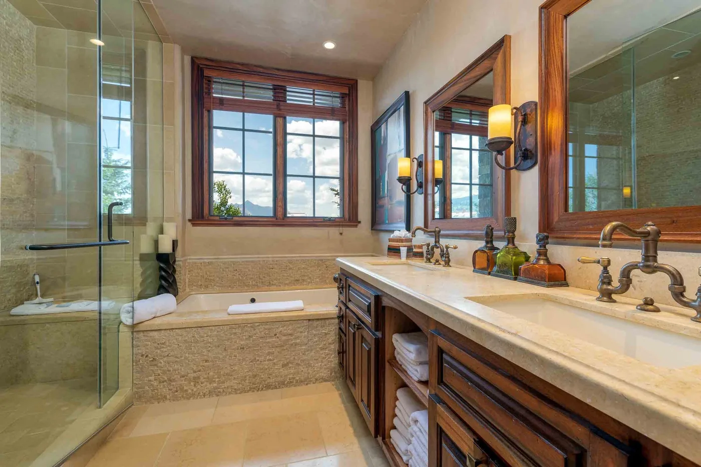 A bathroom with a glass shower, bathtub, and long vanity beneath large mirrors.