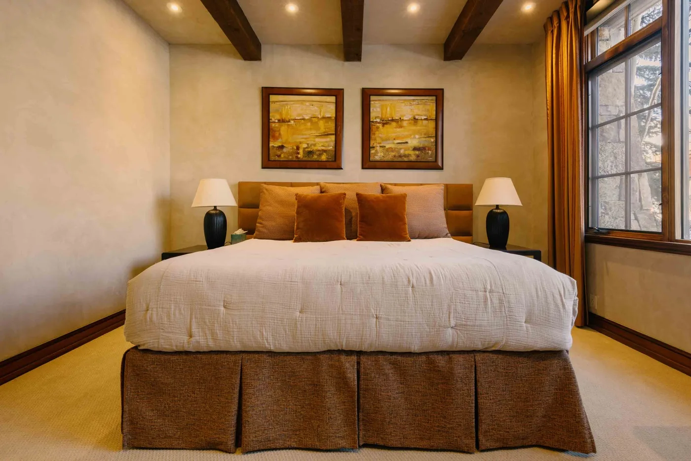 A bedroom with a neatly made bed, matching lamps, and framed artwork above it.