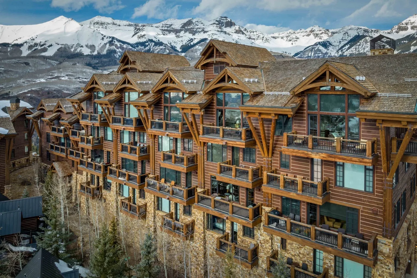 A multi-story timber lodge with balconies stands before snow-covered mountains.