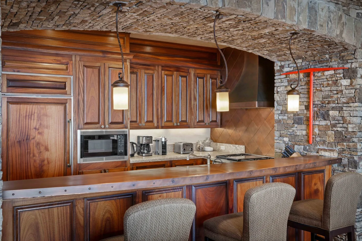 A kitchen with wooden cabinets, a counter, and seating beneath a brick ceiling.