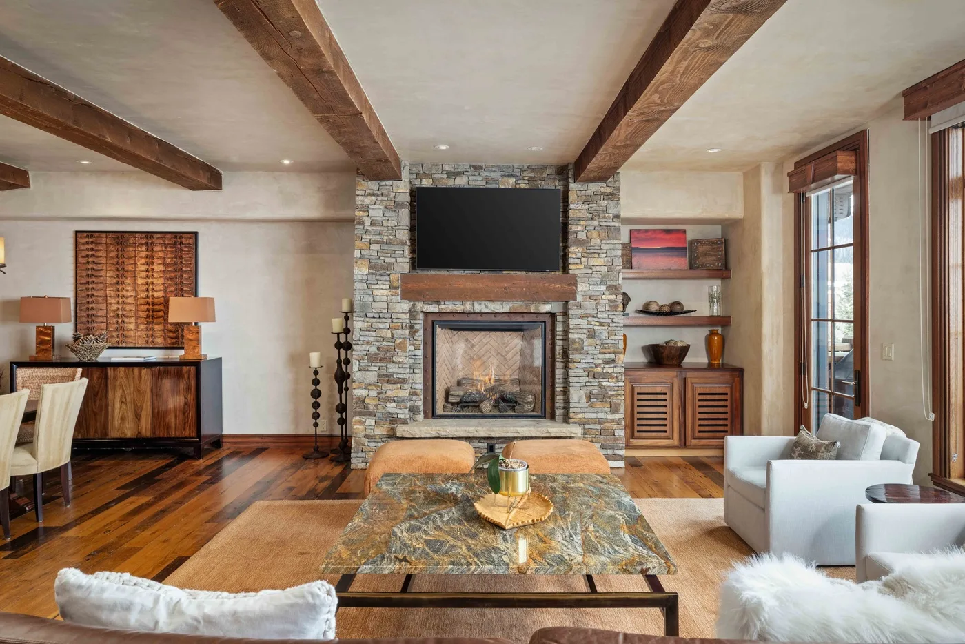 A living room with a stone fireplace, wood ceiling beams, and seating.