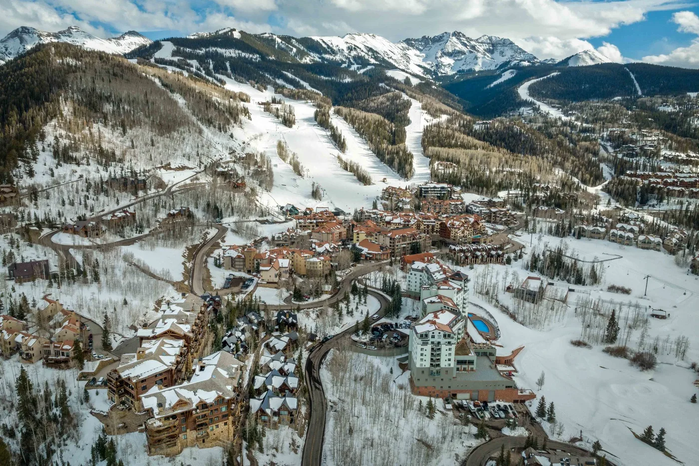 A snow-covered mountain resort sits below ski runs and rugged peaks.