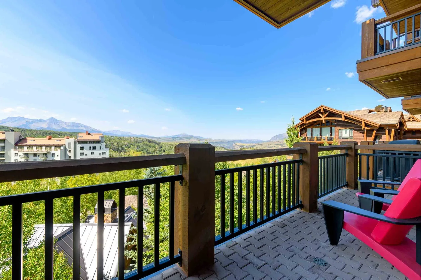 A balcony with outdoor seating overlooks neighboring buildings and a distant mountain landscape.
