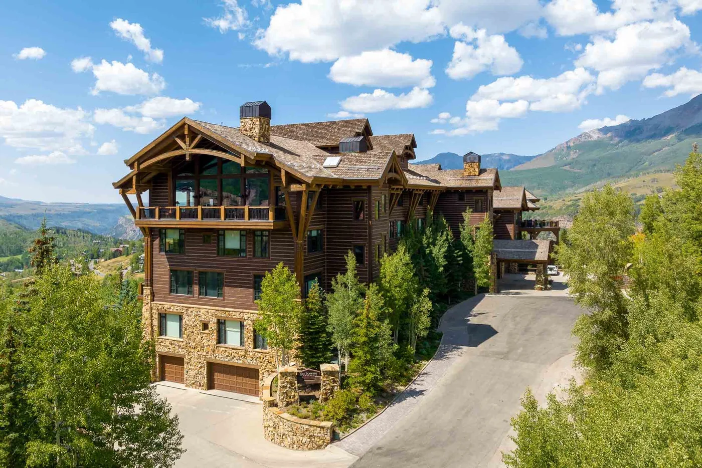 A large lodge stands beside a sloping driveway, with mountains in the background.