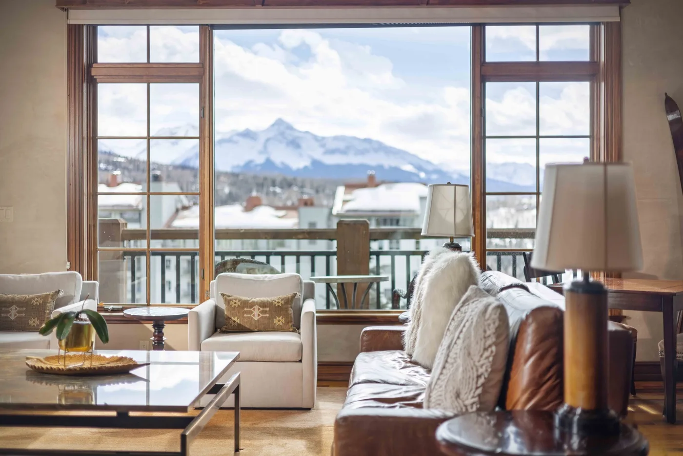 A bright living room with seating beside large windows overlooking snowy mountains.