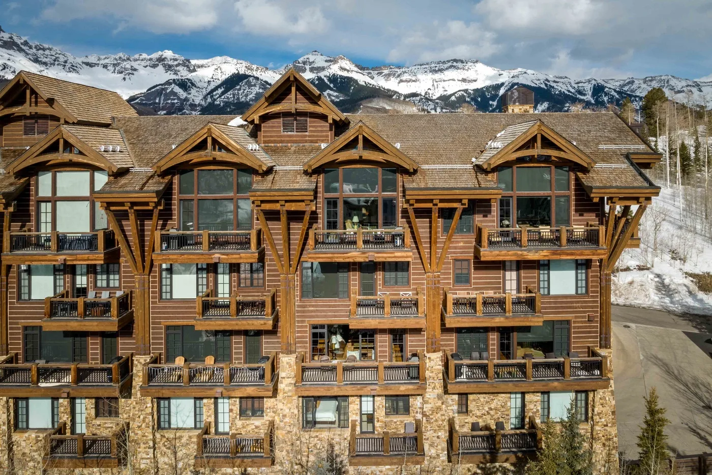 A large timber lodge with balconies stands beneath snow-covered mountains.
