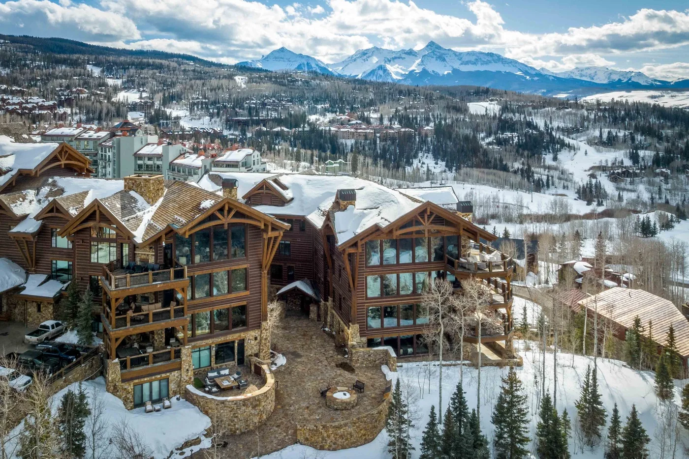 Snow-covered lodge buildings overlook a forested valley and distant mountains.