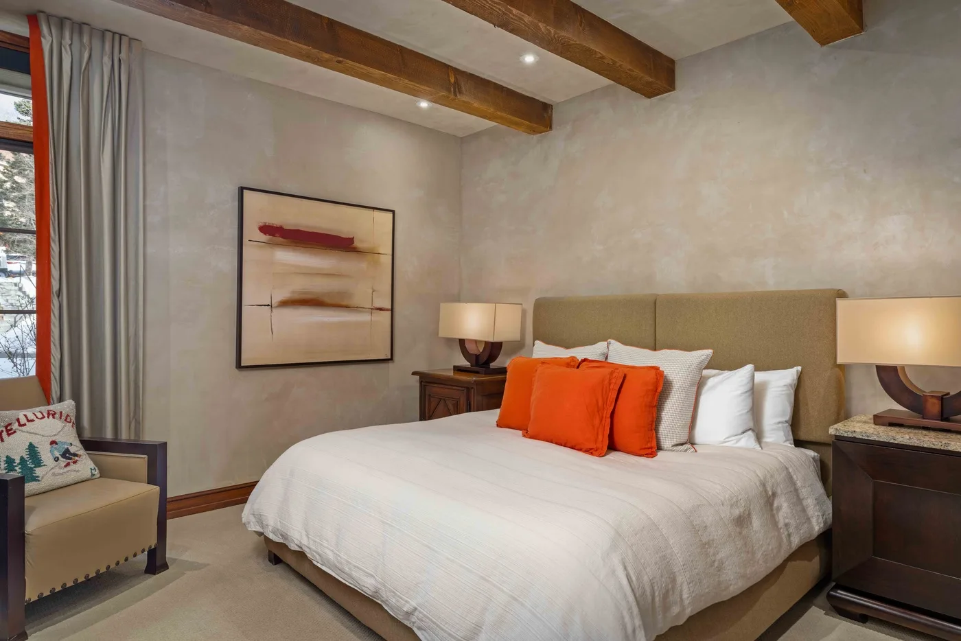 A bedroom with a neatly made bed, orange accent pillows, and bedside lamps.