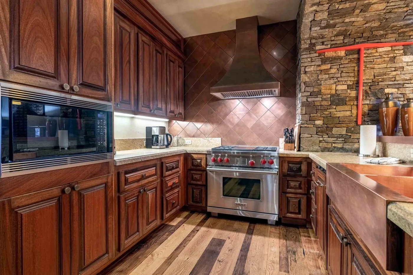 A kitchen with wooden cabinetry, a stainless steel range, and a stone accent wall.