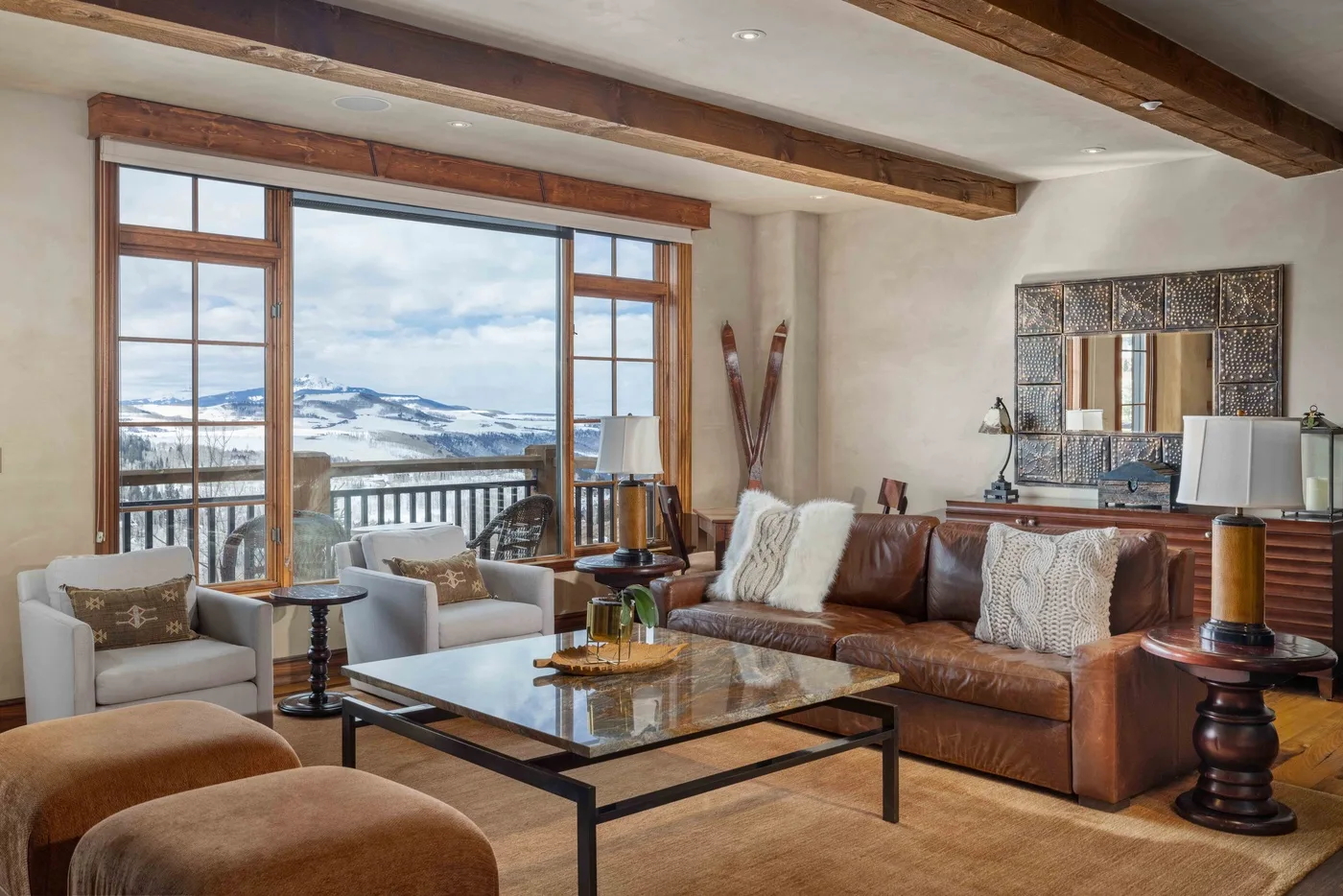 A living room with seating around a coffee table and large windows overlooking a snowy landscape.