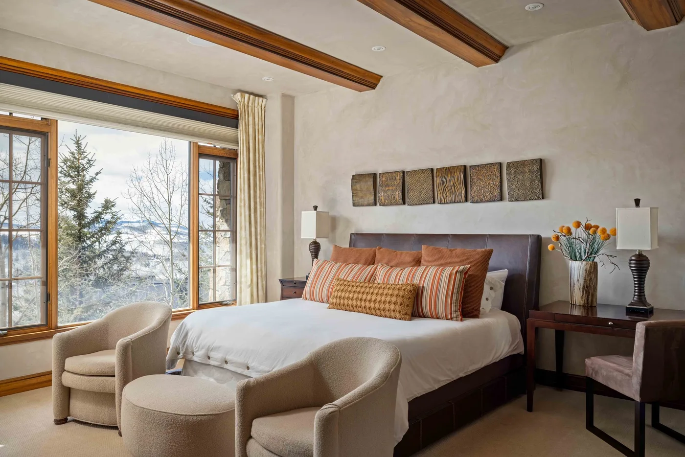 A bedroom with a neatly made bed and large windows overlooking trees.