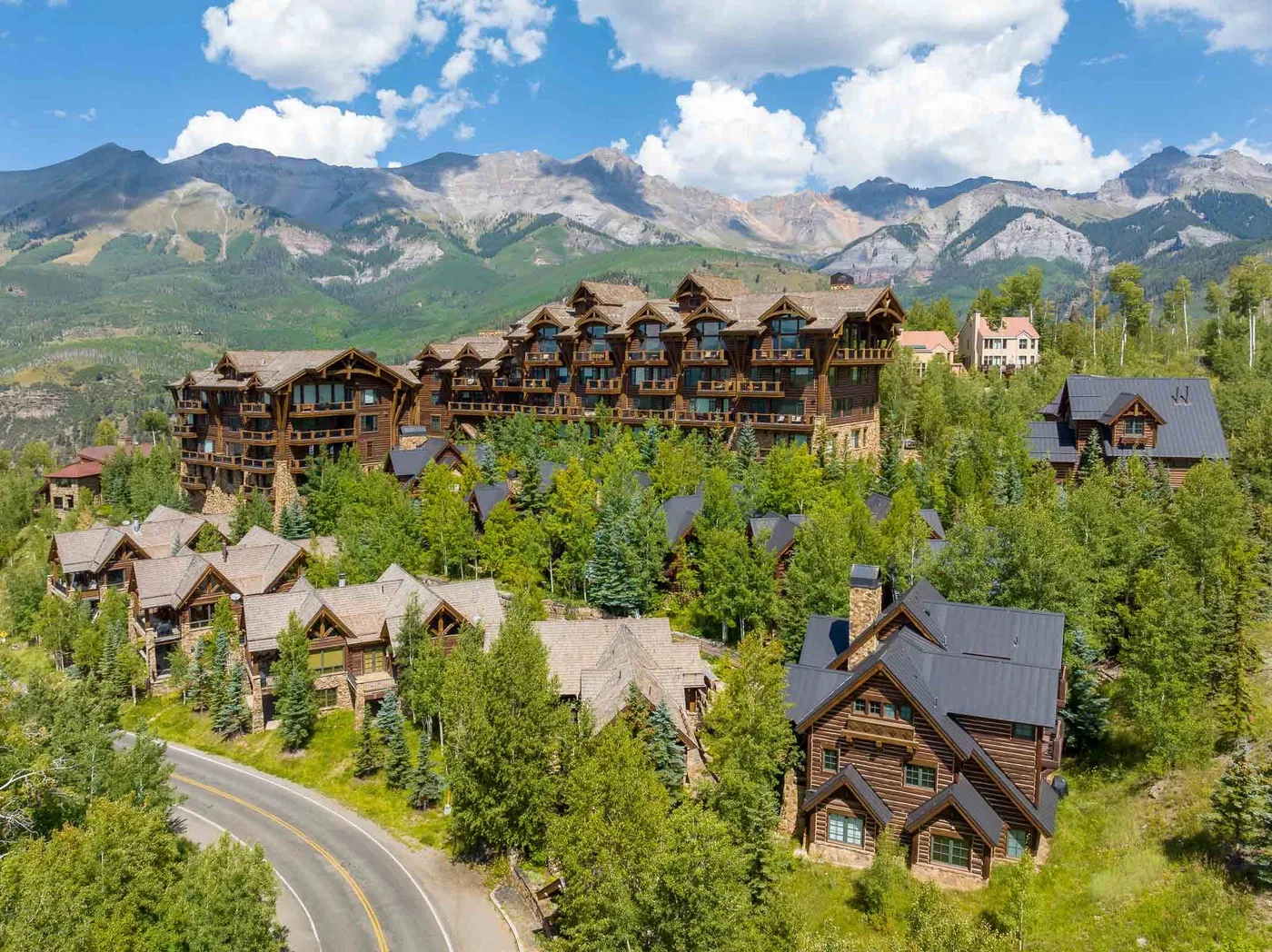 A mountain resort village with timber buildings among trees beneath a rugged mountain range.