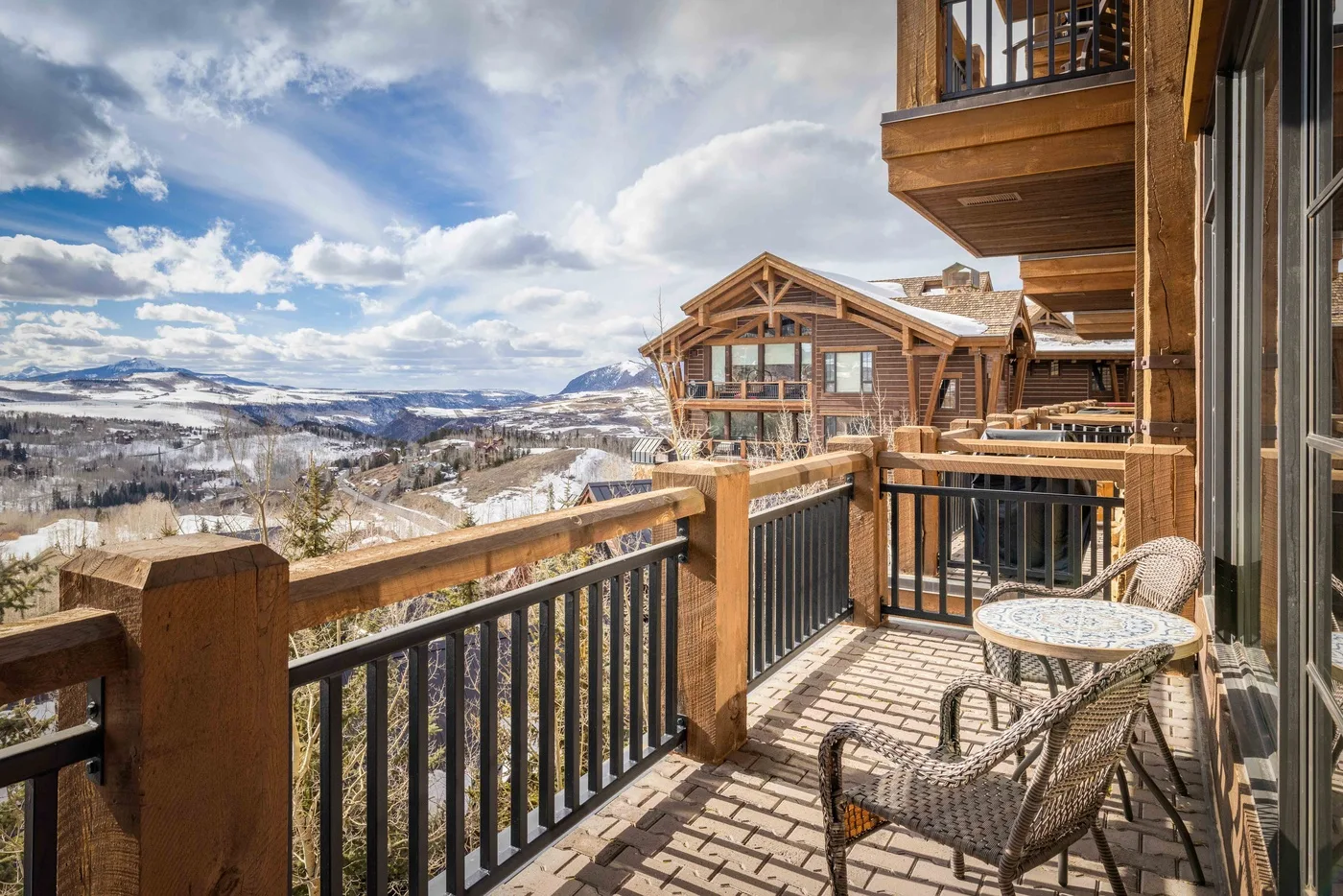 A wooden balcony with outdoor seating overlooks a snowy mountain landscape.