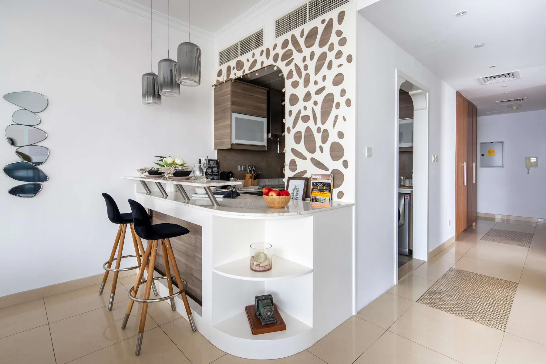 Una cocina pequeña y luminosa con una barra curva y un tabique decorativo junto a un pasillo.