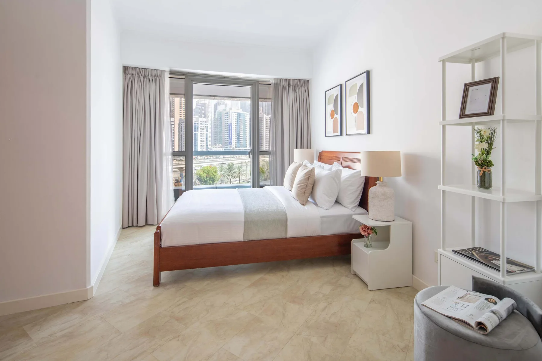 Un dormitorio luminoso con una cama junto a una gran ventana con vistas a edificios de la ciudad.