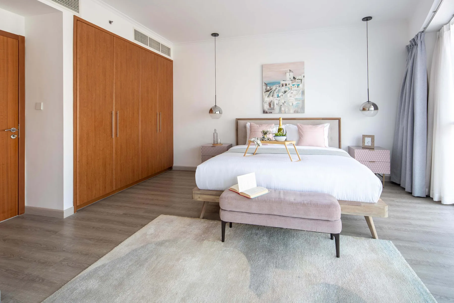 Un dormitorio luminoso con cama, banco tapizado y un gran armario de madera.