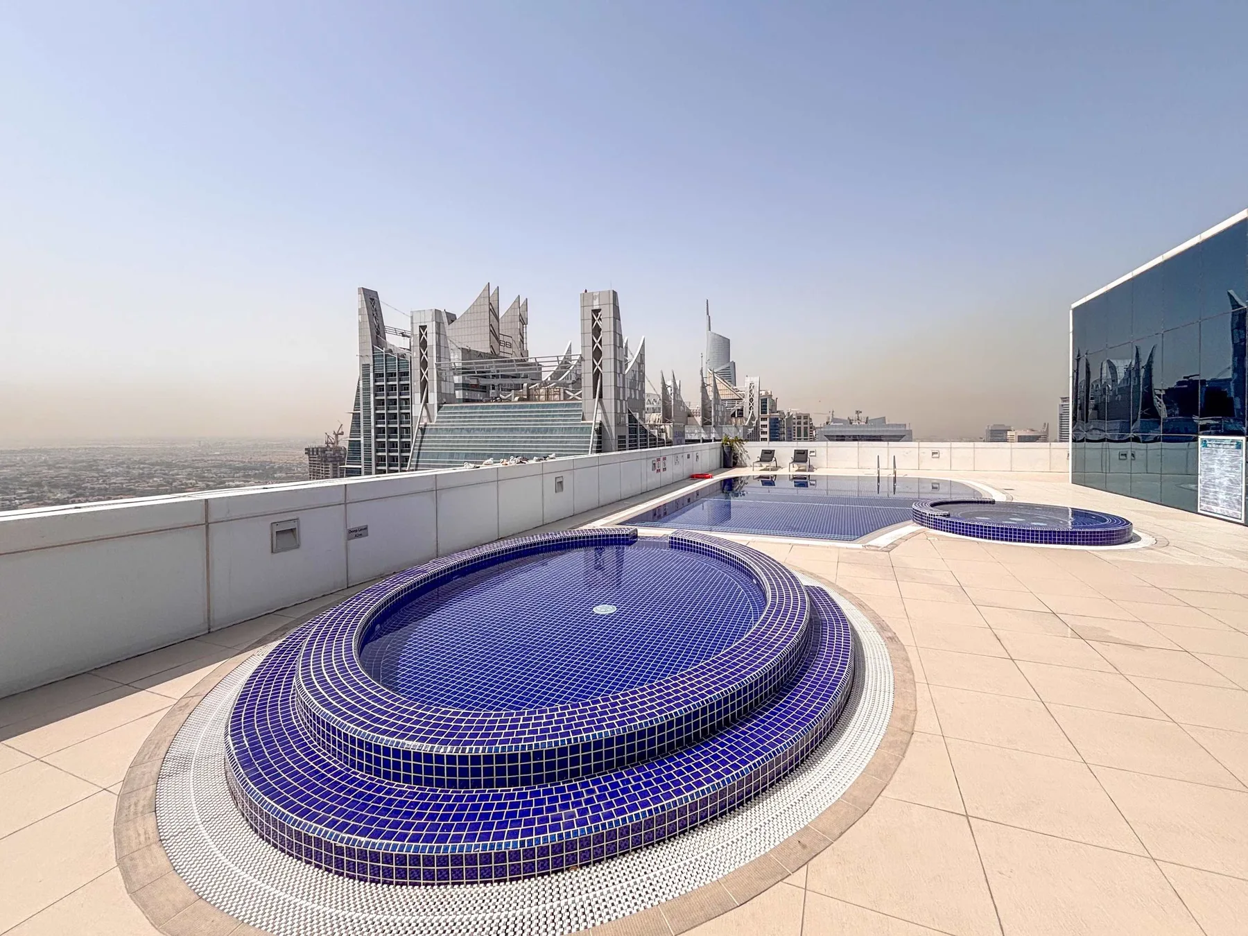 Una terraza en la azotea tiene una gran piscina circular de azulejos junto a edificios modernos.