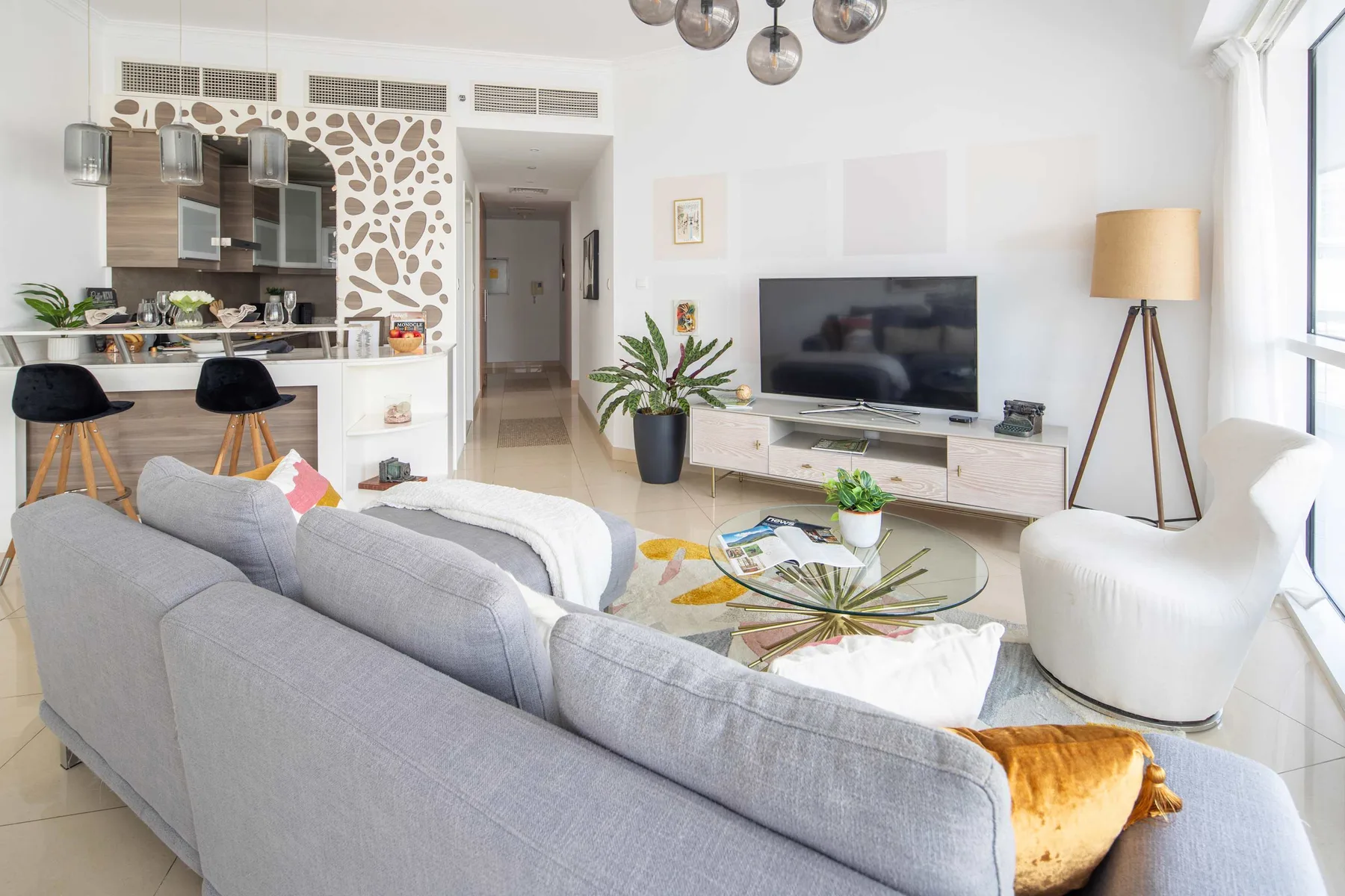 Una sala luminosa con televisor, asientos y una cocina abierta.