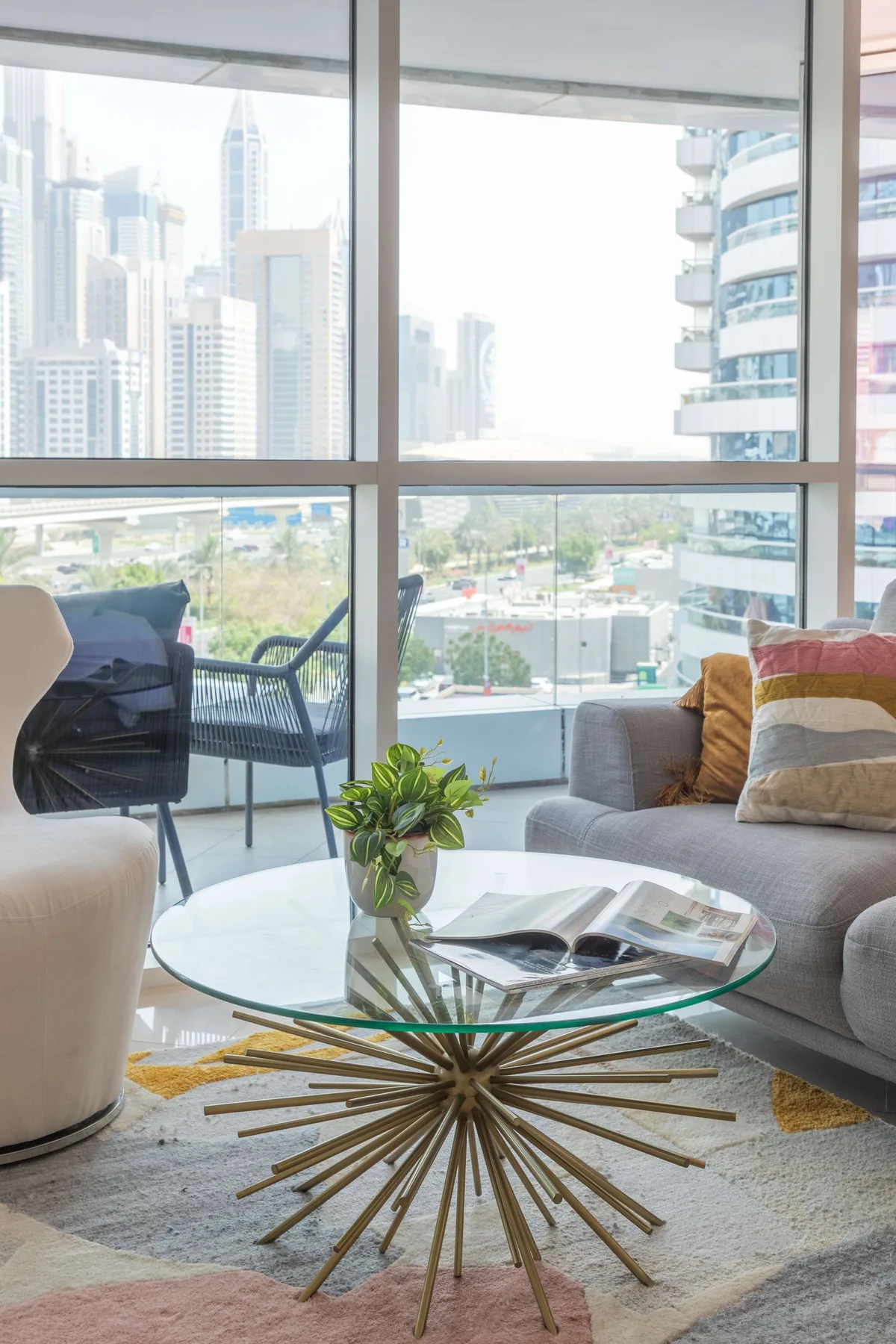 Una sala de estar con asientos, una mesa de centro de vidrio y grandes ventanas con vista a edificios de la ciudad.