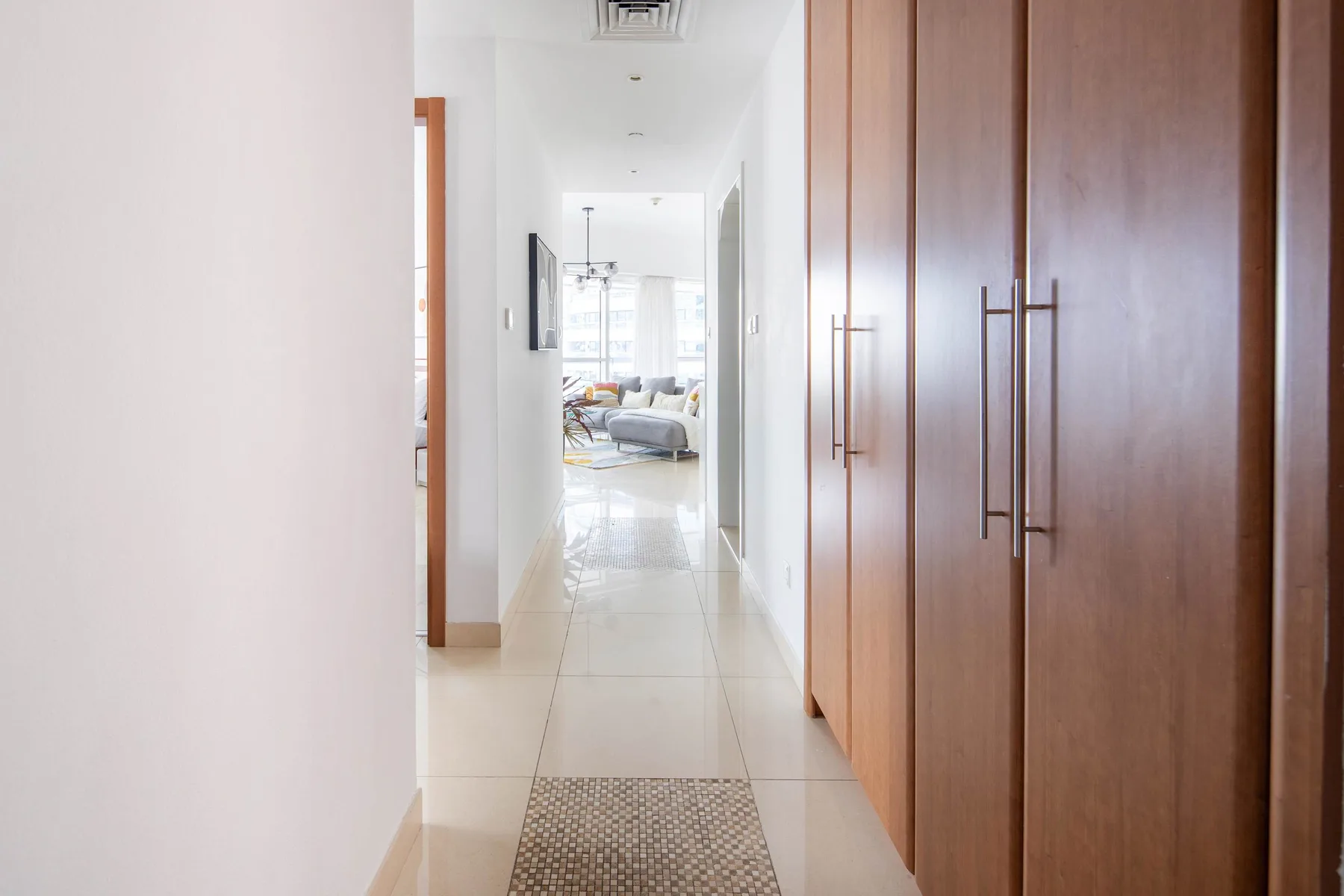 Un pasillo luminoso con armarios de madera altos y una sala de estar al fondo.