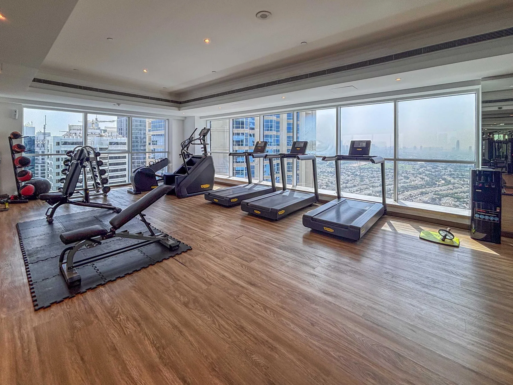 Un gimnasio con máquinas de ejercicio y cintas de correr junto a ventanales.