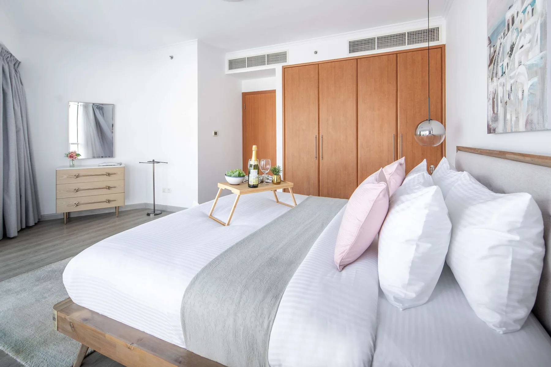 Un dormitorio luminoso con una cama grande, un armario de madera y una mesa pequeña.