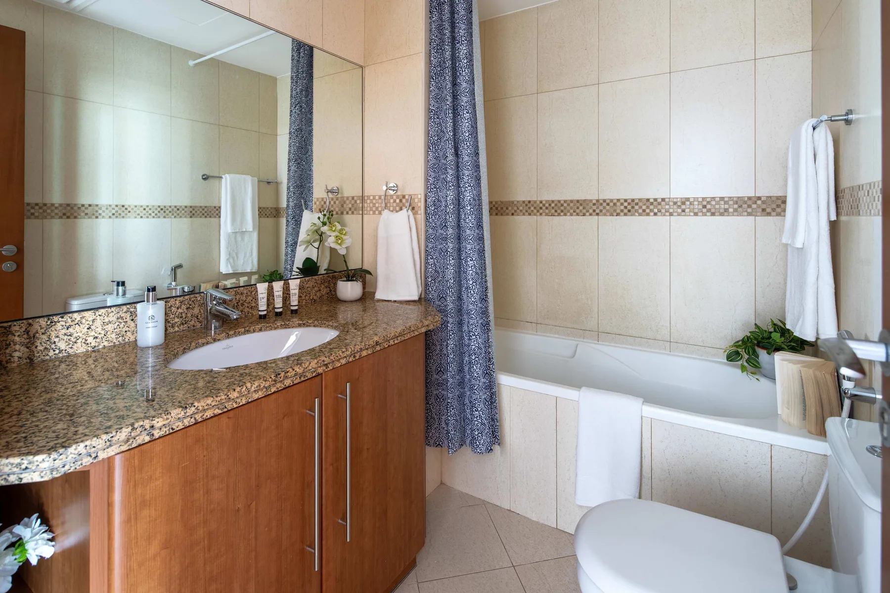 Un baño alicatado con bañera, lavabo y una cortina de ducha estampada.