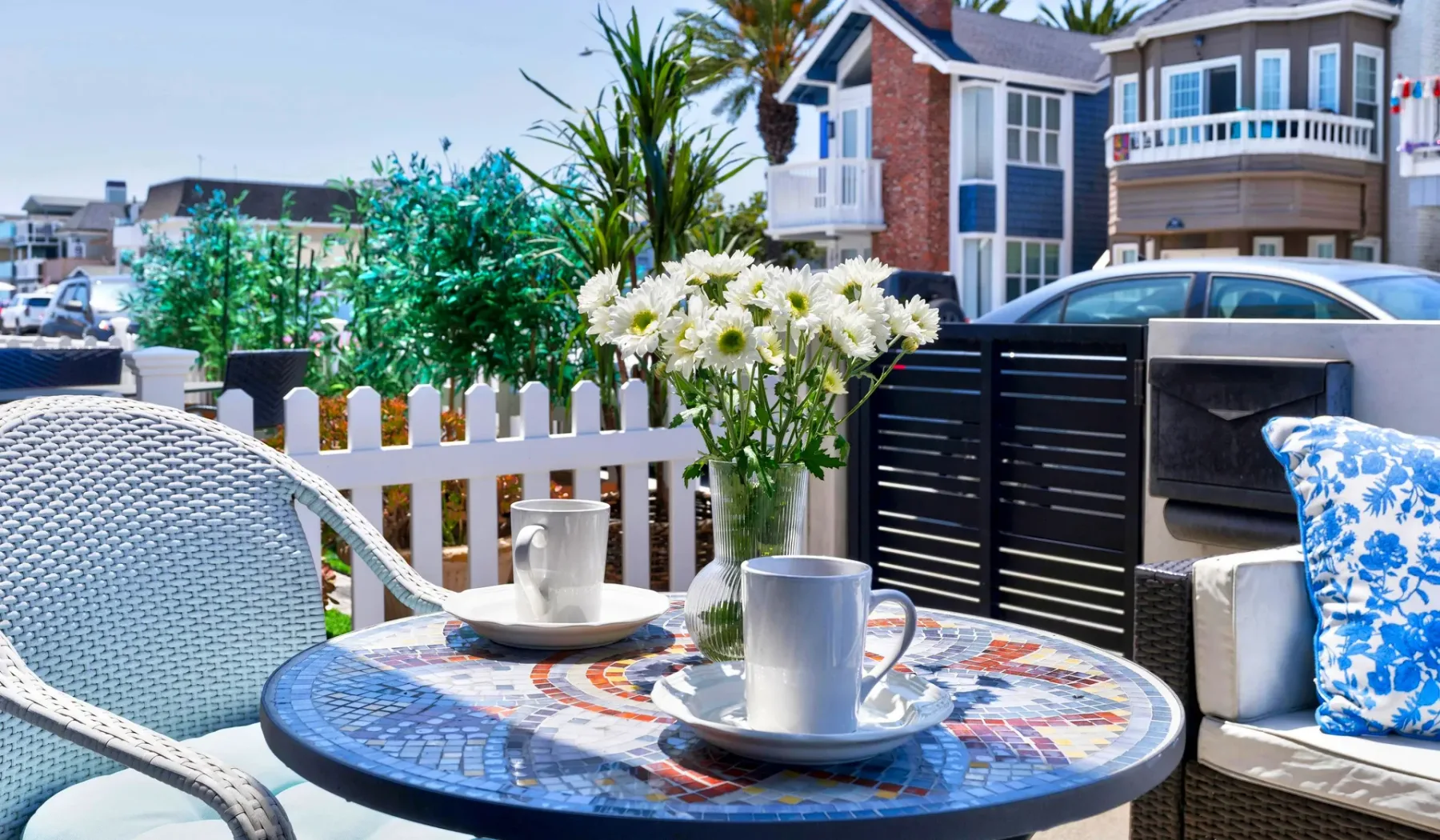 Un patio al aire libre con una mesa redonda, asientos y flores junto a una cerca.