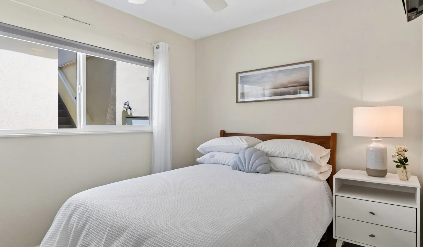 Un dormitorio con una cama bien arreglada, un cuadro en la pared y una lámpara de mesita.