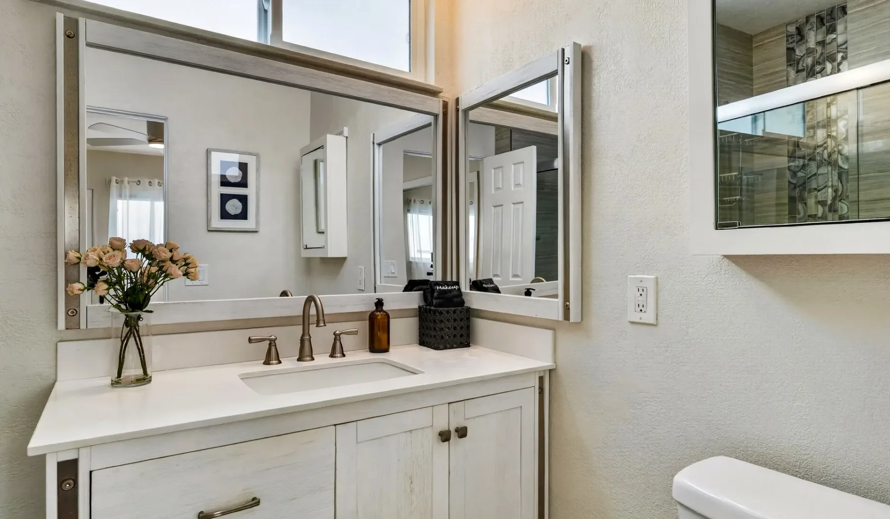 Un tocador de baño con un espejo amplio, lavabo y flores.