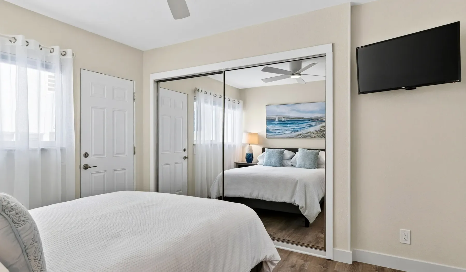 Un dormitorio luminoso con una cama, puertas de armario con espejo y un televisor en la pared.