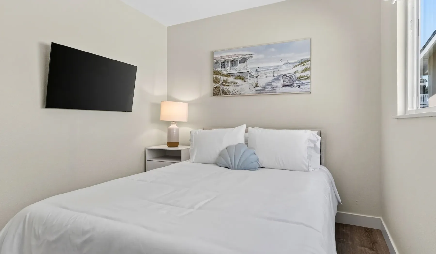 Un dormitorio con una cama tendida, una lámpara de noche y un televisor en la pared.