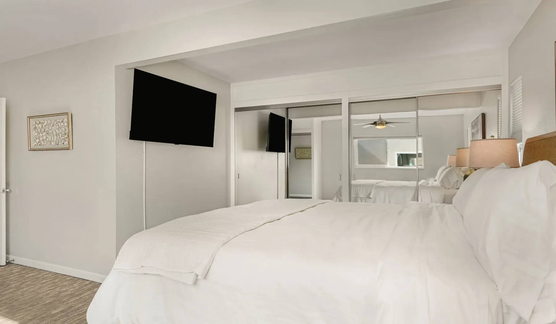 Un dormitorio luminoso con ropa de cama blanca y un televisor en la pared.