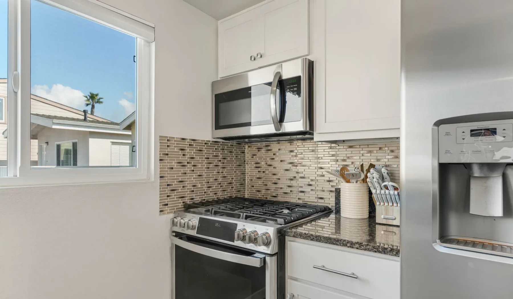 Una cocina luminosa con estufa de gas y una ventana con vista a casas cercanas.