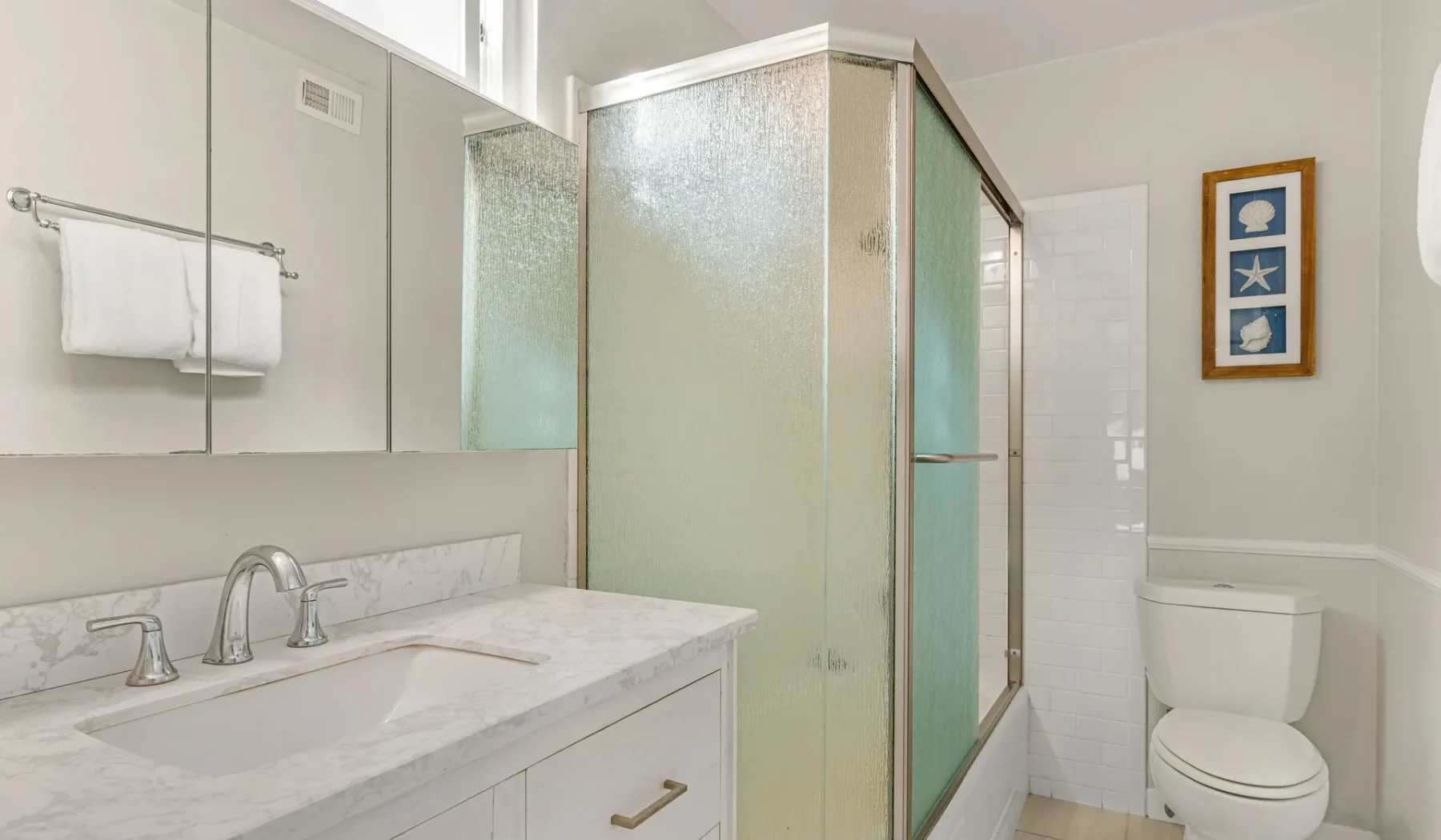 Un baño luminoso con lavabo, ducha de vidrio e inodoro.