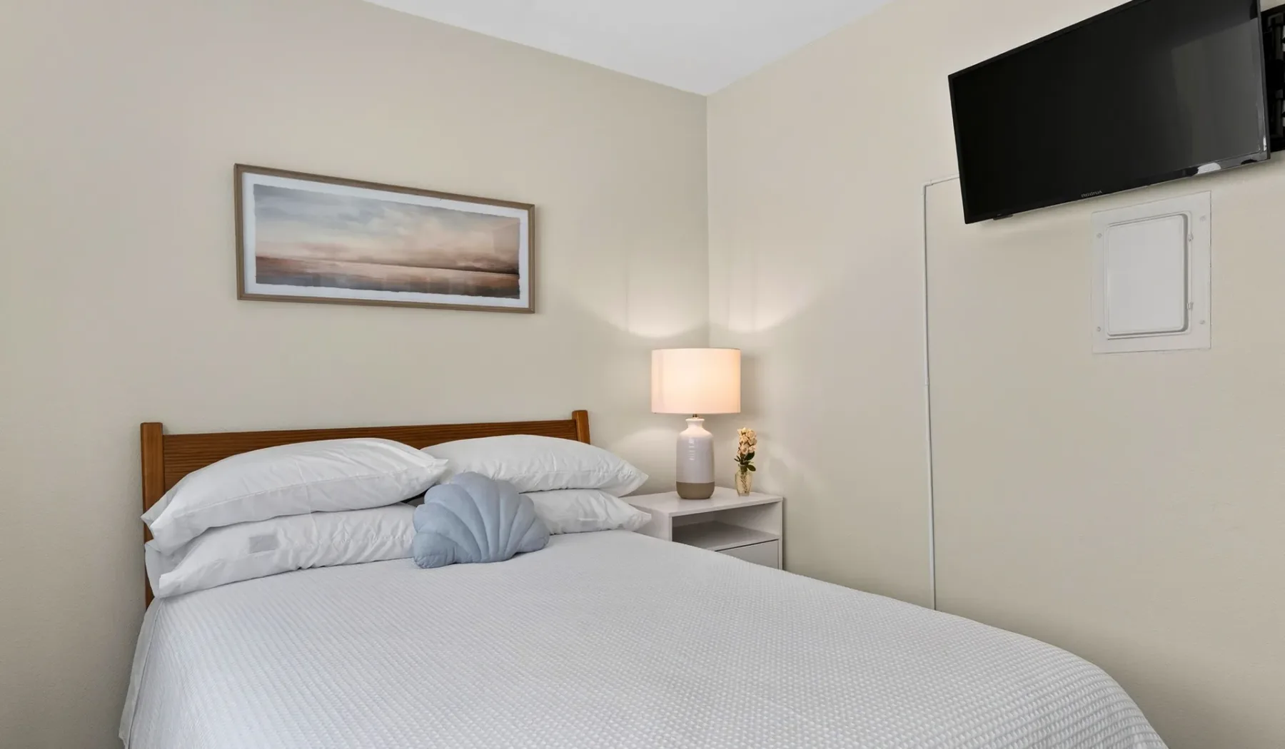 Un dormitorio con una cama tendida y un televisor montado en la pared.