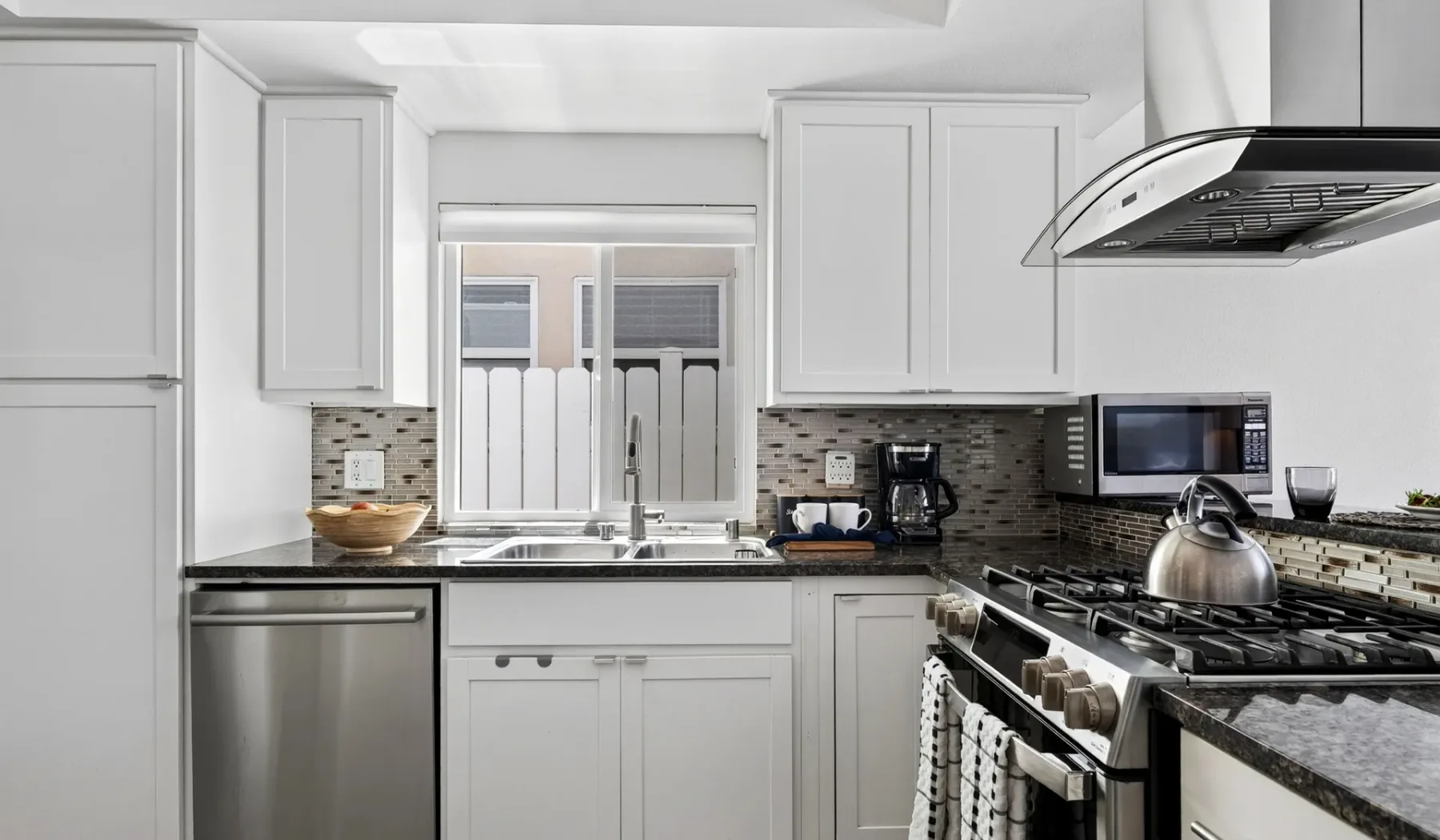 Una cocina luminosa con gabinetes blancos, fregadero y estufa de gas.